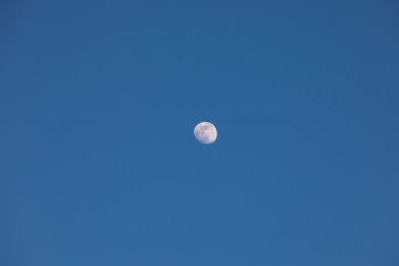 Almost full moon in the in the middle of clear evening sky. Moon as central point of composition. Visible details