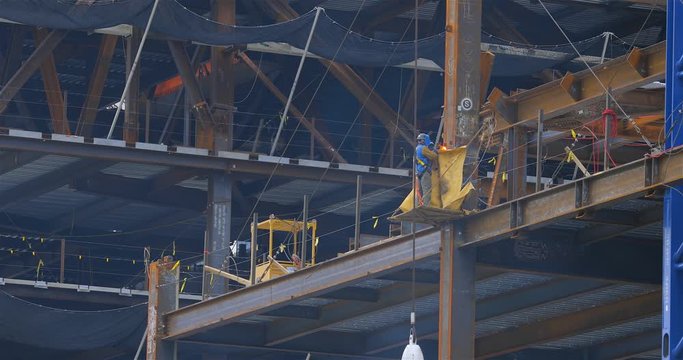 Wide shot of construction workers welding iron structural beams on a high rise building site