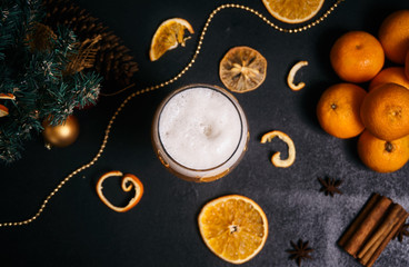 Fototapeta na wymiar a glass of beer with foam on a Christmas background with orange and lemon slices, gold beads and fir branches