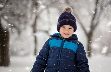 Adorable, cute boy playing with snow cheerfully. Wintertime, kids activity