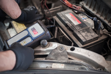 Car mechanic checking and testing automotive accumulator with battery tester