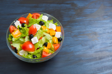 Greek salad in glass bowl on black or dark gray wooden or metal table