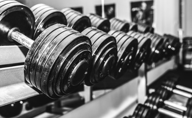 Fototapeta na wymiar Heavy dumbbells lying in the raw in the gym. Fitness sport motivation. Happy healthy lifestyle living. Exercises with bars weights. Black and white photo.