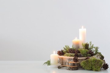 burning candles on saw with cones and branches on white background