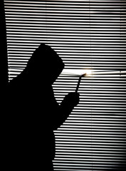 Criminal with crowbar is spying through the window. Old shutter blinds.