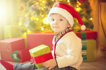 Fototapeta na wymiar Happy little boy with Xmas present on Christmas Eve in decorated room. Sunny morning or day. Christmas or New Year holiday