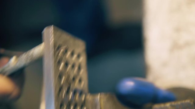 CU: skilled silversmith pulls metal wire through hole in tool with old pliers at workplace in light workshop close view