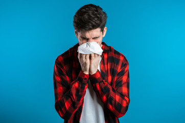 Young man sneezes into tissue. Isolated guy is sick, has a cold or allergic reaction. Health,...