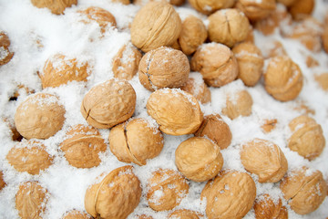 Walnuts are covered in snow at a street market. Illustration of bad weather, unexpected snowfall. Selective focus