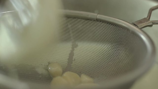 Close up straining garlic onion and bayleaf out of infused milk.
