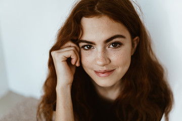 girl with luxurious hair and freckles on her cheeks, gently smiling props her cheek with her hand