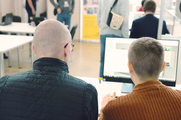 Back view of two male managers or workers look at laptop mock up screen discussing project,...