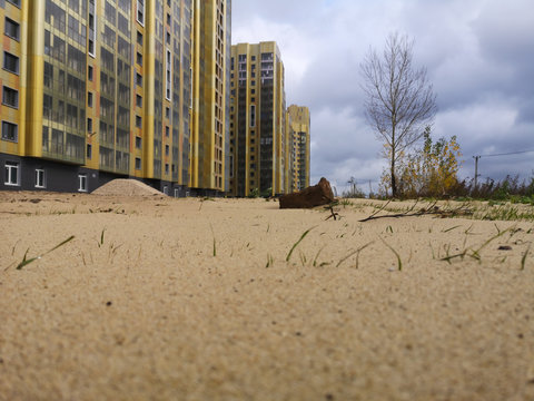 grass on sand in the background of an apartment building sheathed with siding with plastic glazing of windows and balconies