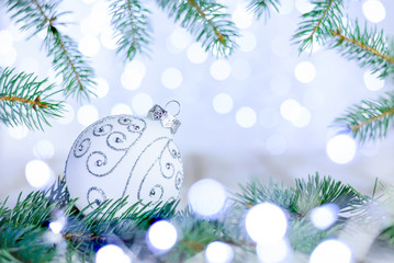 Fototapeta na wymiar Christmas bokeh background with fir branches and white ornate ball. Copy space, soft focus