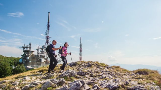 There is a television trasnmitter on top of a mountain. A couple has finally reached the top of the mountain. Weather is really nice.