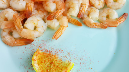 Shrimp served on a blue plate with lemon and red pepper.