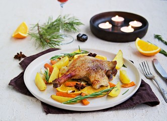 Roasted duck leg with potatoes, carrots and slices of orange on a ceramic plate on a light concrete background. Christmas and New Year dishes recipes. Duck recipes. French cuisine