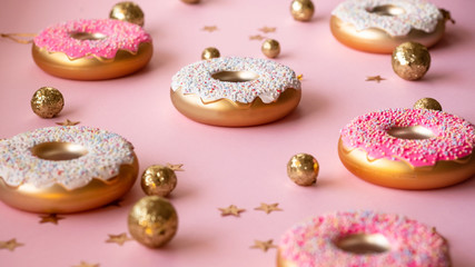 Christmas toys in the form of donuts on a pink background with gold decor, selective focus, side view. Creative food minimalism