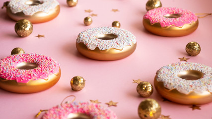 Christmas toys in the form of donuts on a pink background with gold decor, selective focus, side view. Creative food minimalism