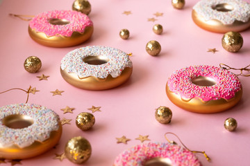 Christmas toys in the form of donuts on a pink background with gold decor, selective focus, side view. Creative food minimalism