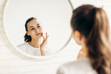 The woman is making up in the bathroom. Woman in bathroom applying cream on face.