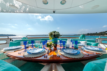Ocean-themed table setting with blue plates, wine glasses and a flower bouquet on a luxury yacht