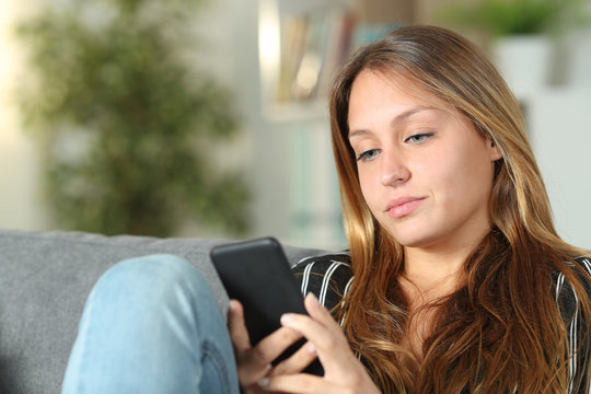 Serious woman using mobile phone on a sofa at home
