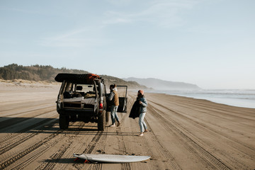 Two people on the beach with their car
