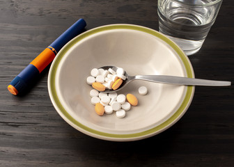 Diabetes theme. A bowl with medication in a spoon, accompany by a insulin syringe and a glass of water.