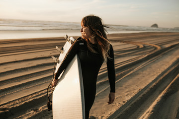 Naklejka premium Uśmiechnięta kobieta z deską surfingową spaceru na plaży podczas zachodu słońca