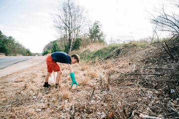 little boy picking up trash on the side of the road for earth day
