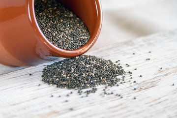 Edible seeds of chia, Salvia hispanica, a flowering plant of the mint family. A popular healthy food product. Chia seeds are poured from a brown clay pot. Blurred.