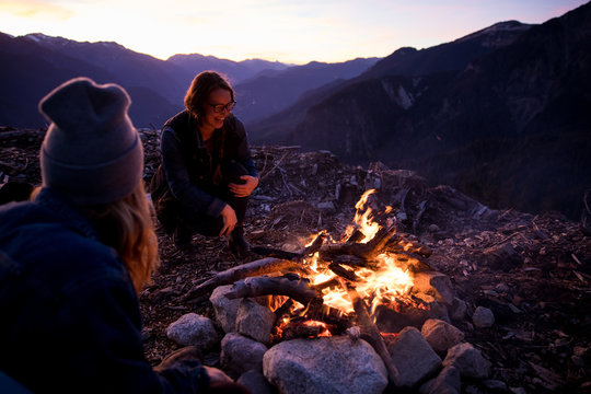 Friends warming around a bonfire at dusk in the mountains