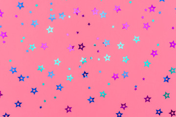 Photo of multi-colored stars glitter sprinkles on pink background. Festive holiday background for your projects. Celebration concept. Christmas pattern. Top view, flat lay