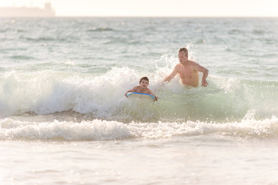 Dad launching his son onto a wave in low surf at the beach