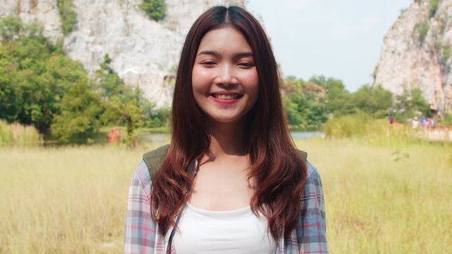 Cheerful young traveler Asian lady with backpack feeling happy smiling to camera at mountain lake. Korean girl enjoy her holidays adventure feeling happy freedom. Lifestyle travel and relax concept.
