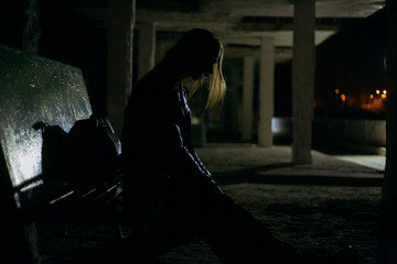 dark silhouette of a sad girl sitting on a bench in a depressive pose
