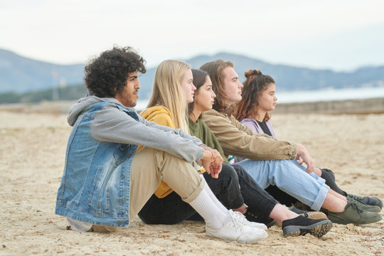 Cool dreaming teenagers sitting on sand
