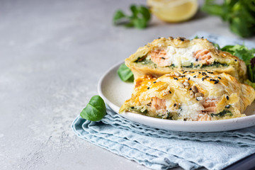 Puff pastry pie with salmon, spinach and ricotta cheese served with green lettuce leaves. Salmon...