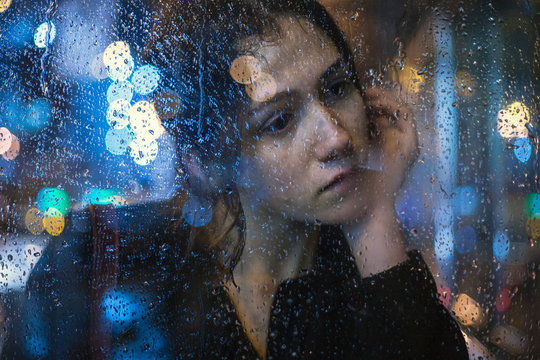 atmospheric portrait of a girl through the glass through which rainwater flows with a beautiful bokeh