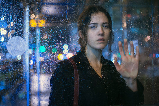 Portrait of young woman looking through wet glass