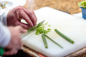 High angle shot of a person cutting green onions on a white chopping board