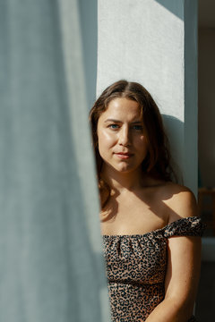 Portrait of young woman standing in sunlight behind curtain