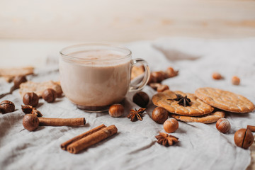 Hot cocoa with cookies, cinnamon sticks, anise, nuts on wooden background. Front view.