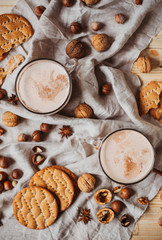 Hot cocoa with cookies, cinnamon sticks, anise, nuts on wooden background. Top view.