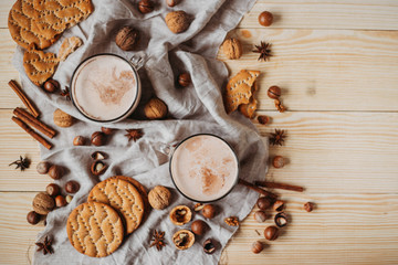 Hot cocoa with cookies, cinnamon sticks, anise, nuts on wooden background. Top view, copy space.