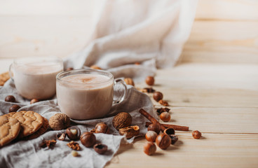 Hot cocoa with cookies, cinnamon sticks, anise, nuts on wooden background. Front view.