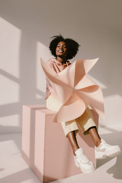 Cheerful black woman with pinwheel sitting on cube