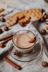 Hot cocoa with cookies, cinnamon sticks, anise, nuts on wooden background. 