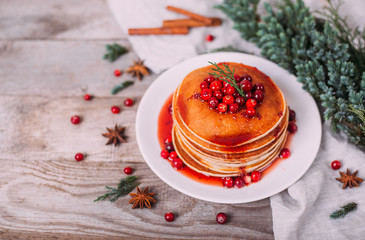 Stack of american pancakes with fresh cranberry and jam in white plate on wooden rustic table decorated Christmas tree, delicious dessert for breakfast in winter, vintage style. 